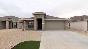A residential house with a garage, a driveway, and a well-maintained lawn. - Auburn House - New 4BR Near Texas Tech (Lubbock)