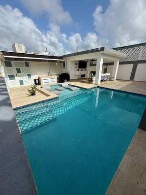 A swimming pool with a tiled deck, a covered seating area, and a white exterior wall. - Villa Valmira | private pool (Canóvanas)