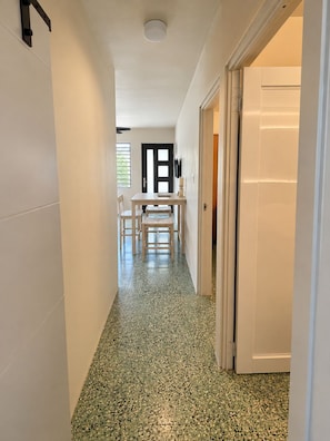 Ein Flur mit einer Tür zu einem Zimmer, einem Tisch mit Stühlen und einem Fenster mit Jalousien.