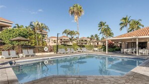 A pool area with lounge chairs and umbrellas, surrounded by palm trees and buildings with tiled roofs. - Luxury 2BR Plus Suite on Hawaii's Kohala Coast Near Golf & Beaches (Waikoloa Village)