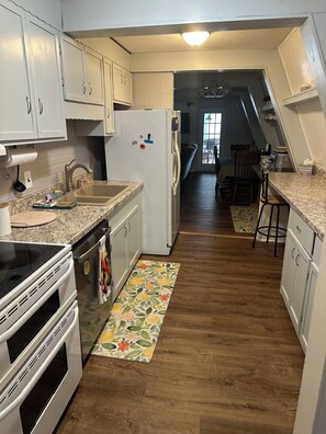 A kitchen with white cabinets, a granite countertop, a refrigerator, a stove, and a wooden floor. - 3-bedroom cottage on the water in peaceful Hollywood with AC for relaxing stays (Hollywood)