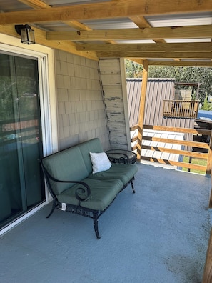A covered patio area with a green cushioned bench, a glass door, and a wooden fence in the background. - 3-bedroom cottage on the water in peaceful Hollywood with AC for relaxing stays (Hollywood)
