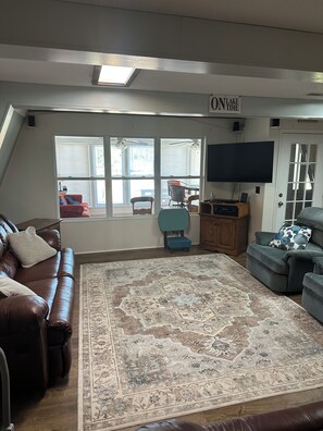 A living room with a large rug, leather sofas, a flat-screen TV, and a sign that reads 'ON LAKE TIME'. - 3-bedroom cottage on the water in peaceful Hollywood with AC for relaxing stays (Hollywood)
