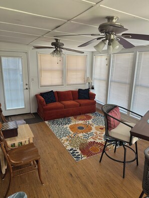A living room with a red sofa, a wooden coffee table, a patterned rug, and two ceiling fans. - 3-bedroom cottage on the water in peaceful Hollywood with AC for relaxing stays (Hollywood)