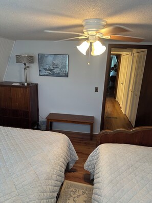 Ein Schlafzimmer mit zwei Betten, einem Deckenventilator, einem Nachttisch, einer Bank, einer Wandlampe und einem Gemälde.