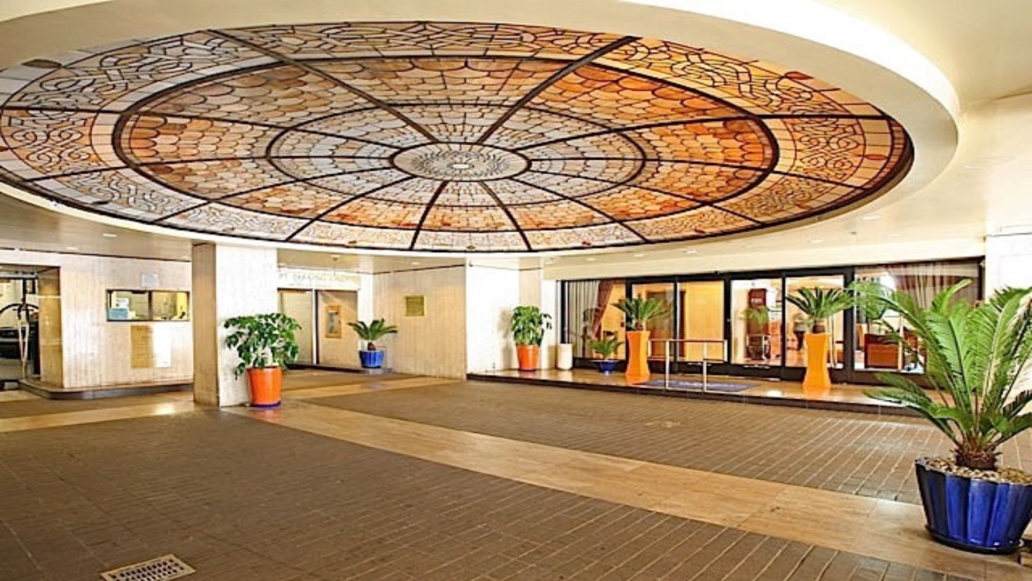 A spacious lobby with a large, ornate ceiling and potted plants.