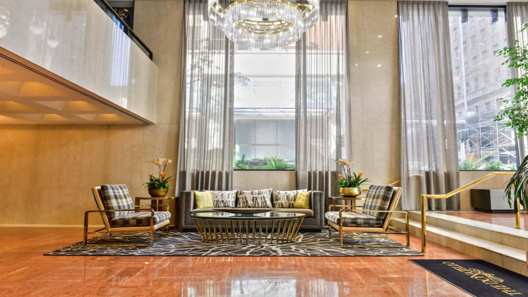 A spacious lobby with a modern sofa set, a chandelier, and a view of the cityscape through large windows.
