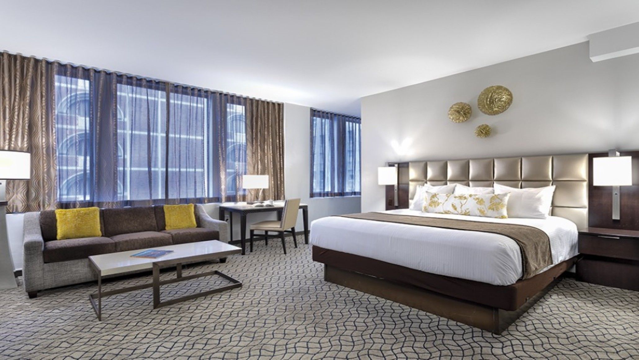 A hotel room with a large bed, a sofa, a desk, and a chair.