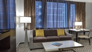A hotel room with a sofa, two lamps, a coffee table, and a TV.