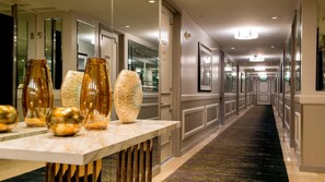Un couloir d’hôtel avec un comptoir de réception en marbre, de grands vases et des œuvres d’art encadrées accrochées aux murs.