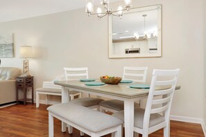 Un comedor con una mesa de madera, sillas blancas, un banco e intensidor.