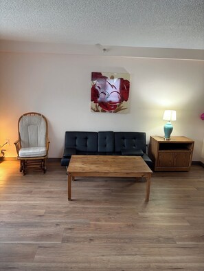 A living room with a wooden coffee table, a dark sofa, a wooden chair, a lamp, and a painting on the wall. - Comfortable 2Bed 1Bath Condo in Auburn (Auburn)