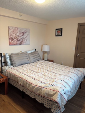 A bedroom with a bed, a nightstand, a lamp, a framed picture, and a door. - Comfortable 2Bed 1Bath Condo in Auburn (Auburn)