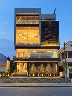 A modern hotel with a two-story structure, large glass windows on the upper floor, and a sign indicating it is a Kingstont Suites hotel. - Kingston Suites (Mysore)