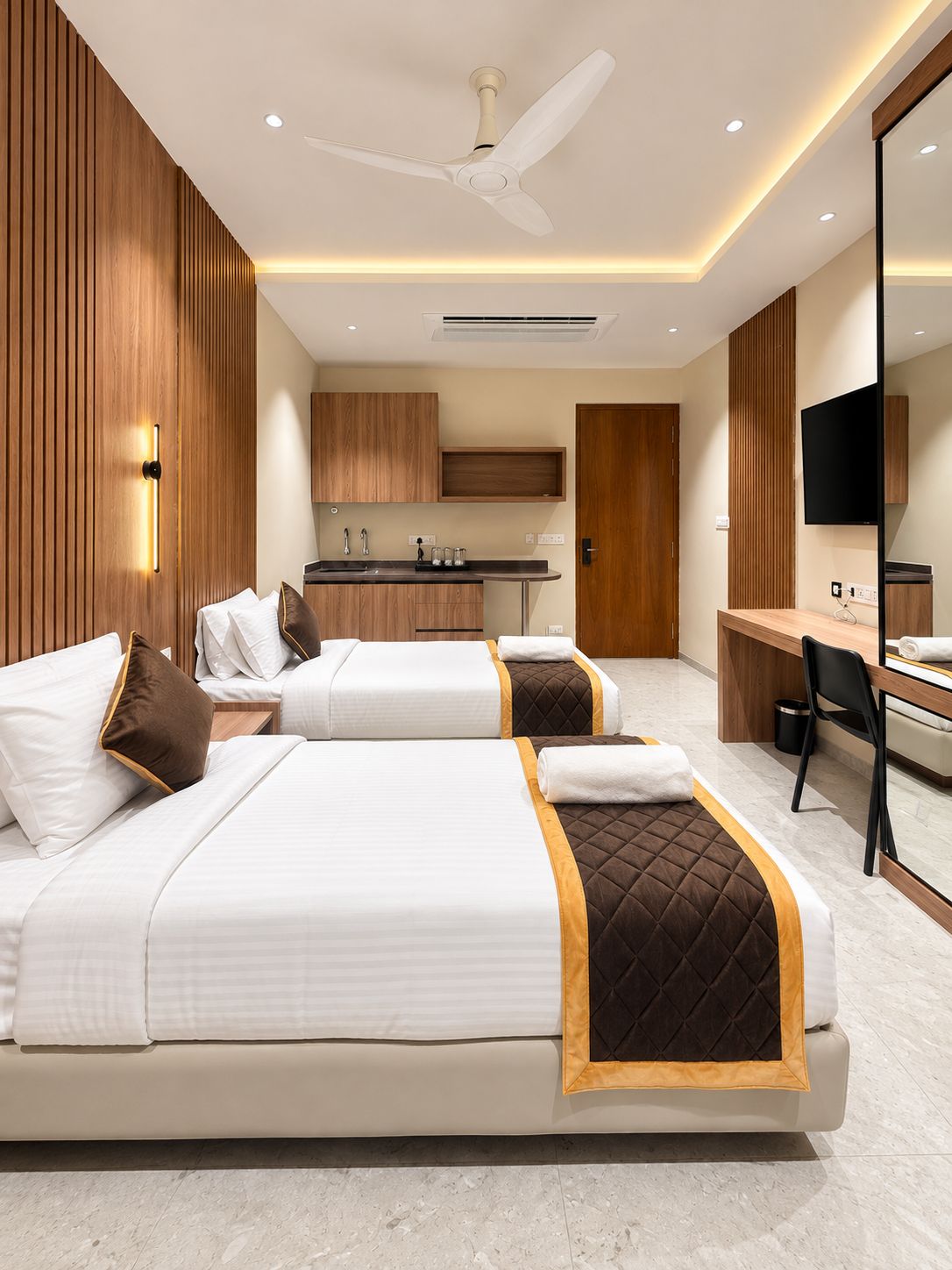 A hotel room with two beds, a desk, a chair, a TV, and a kitchenette.