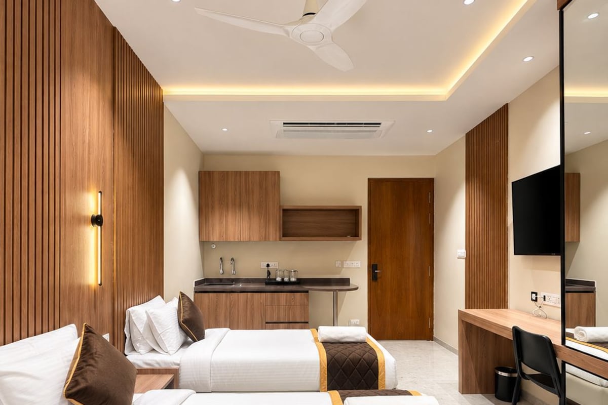 Habitación de hotel con dos camas, un escritorio, una silla, un televisor y una kitchenette.
