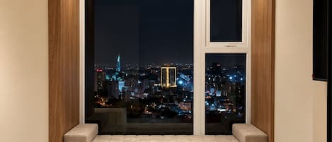 A modern hotel room with a large window, a bed, a desk, and a chair.