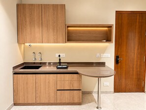 A modern kitchen with wooden cabinets, a stainless steel sink, and a built-in oven. - Kingston Suites (Mysore)