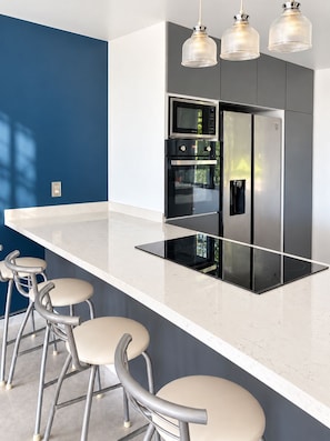 A modern kitchen with a central island, stainless steel appliances, and bar stools. - Vrbo Property (Fraccionamiento Lomas de Cocoyoc)