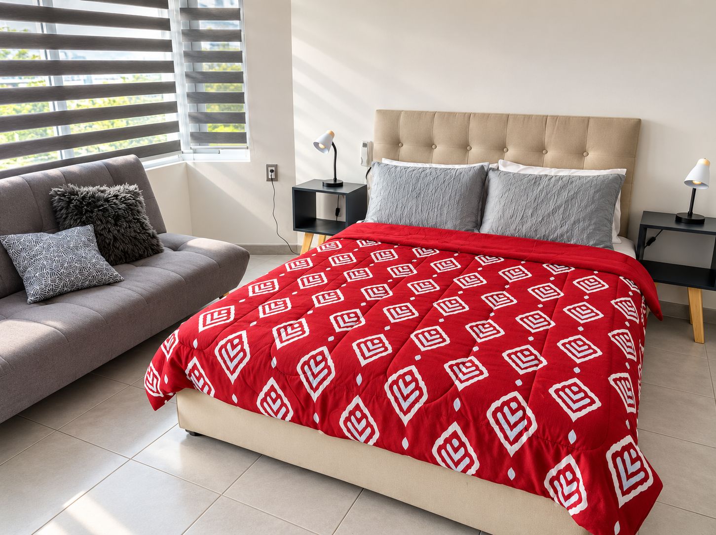 A bedroom with a bed, a sofa, a nightstand, and a lamp.