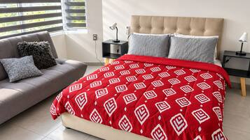 A bedroom with a bed, a sofa, a nightstand, and a lamp.