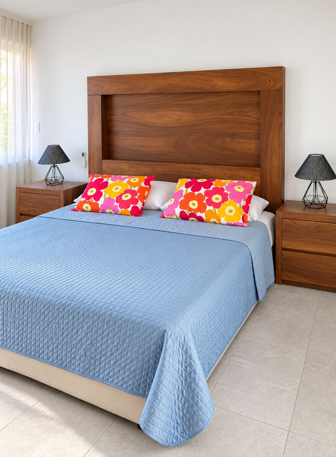 A bed with a blue quilt, two wooden nightstands, a wooden headboard, and two lamps.