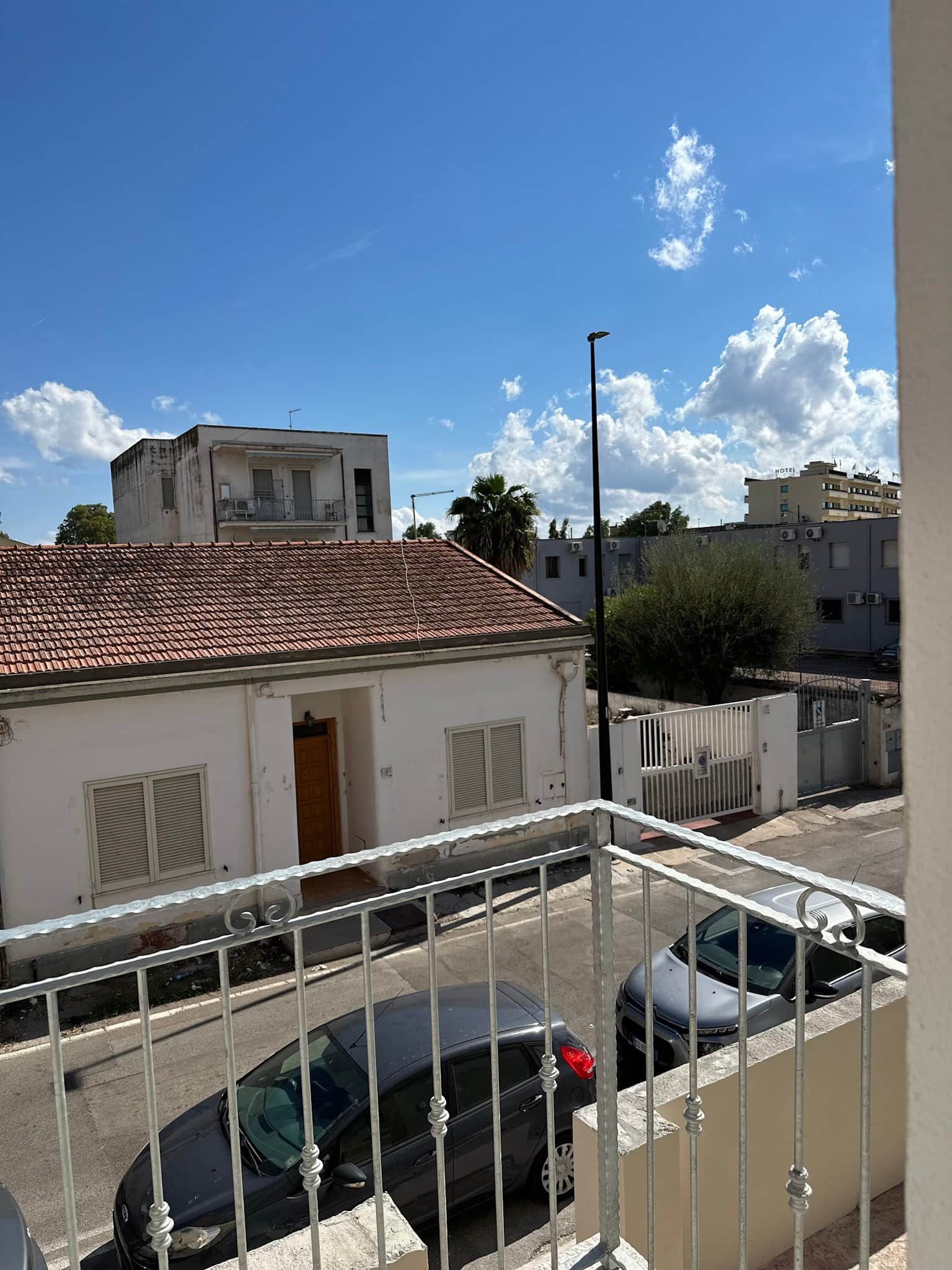 A residential building with a tiled roof, a balcony with a metal railing, and a parked car in the foreground.