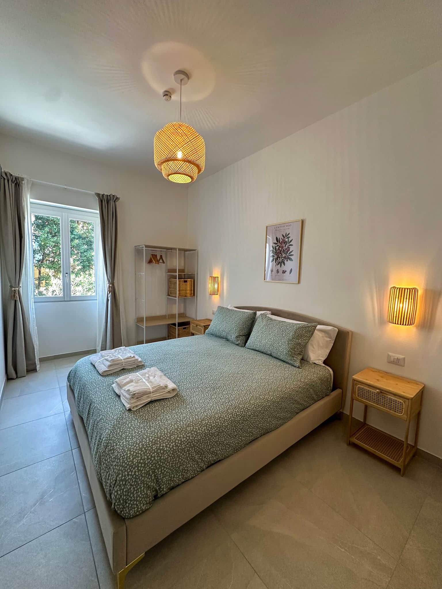 A bedroom with a bed, a bedside table, a lamp, a wardrobe, and a window with curtains.