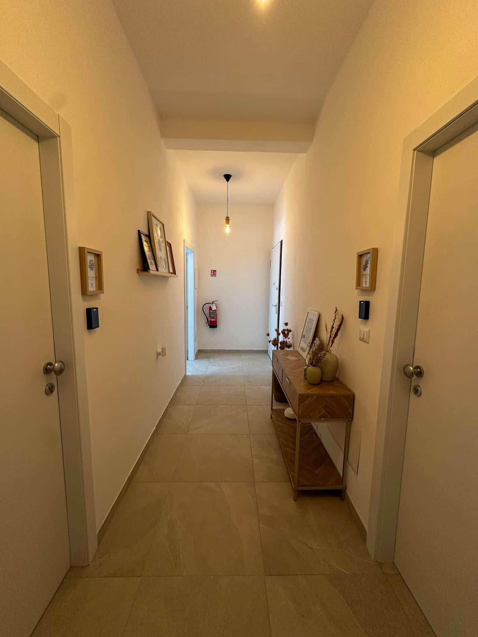 A hallway with a wooden bench, framed pictures, and a fire extinguisher.