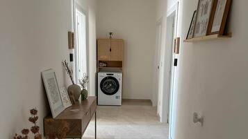 A hallway with a washing machine, a wooden bench with decorative items, and framed pictures on the walls.
