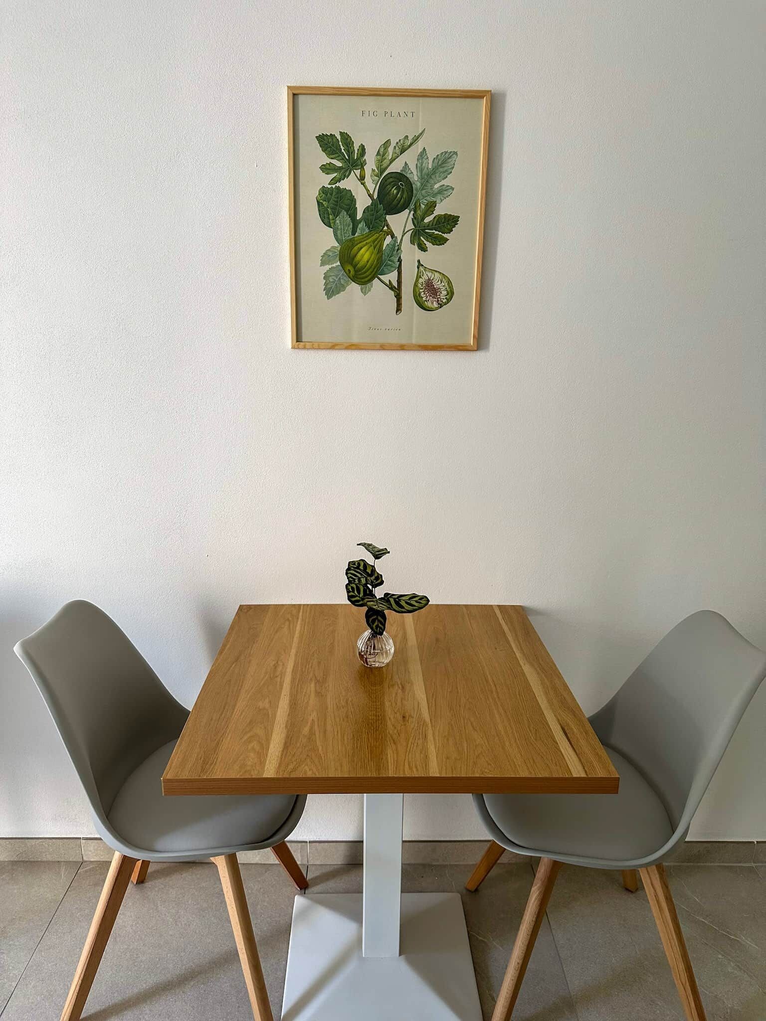 A dining table with two chairs, a framed botanical illustration, and a decorative glass object.