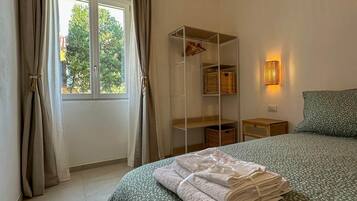 A bedroom with a bed, a window with curtains, a bedside table, and a wall-mounted lamp.