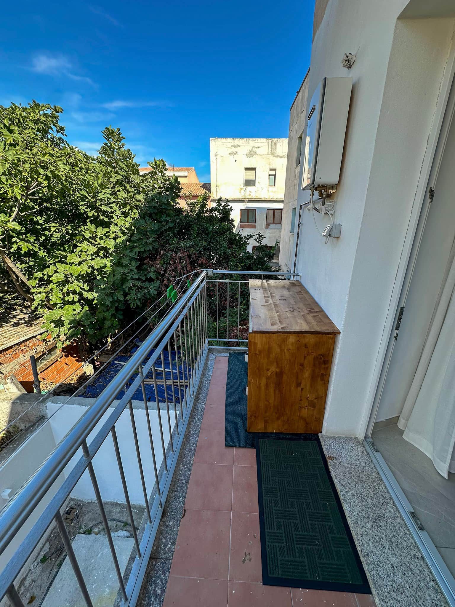 A narrow balcony with a wooden ledge, a metal railing, and a door with a mat.