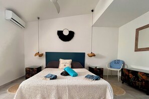 Un dormitori amb un llit, una làmpada penjant, una cadira i un mirall fixat a la paret.