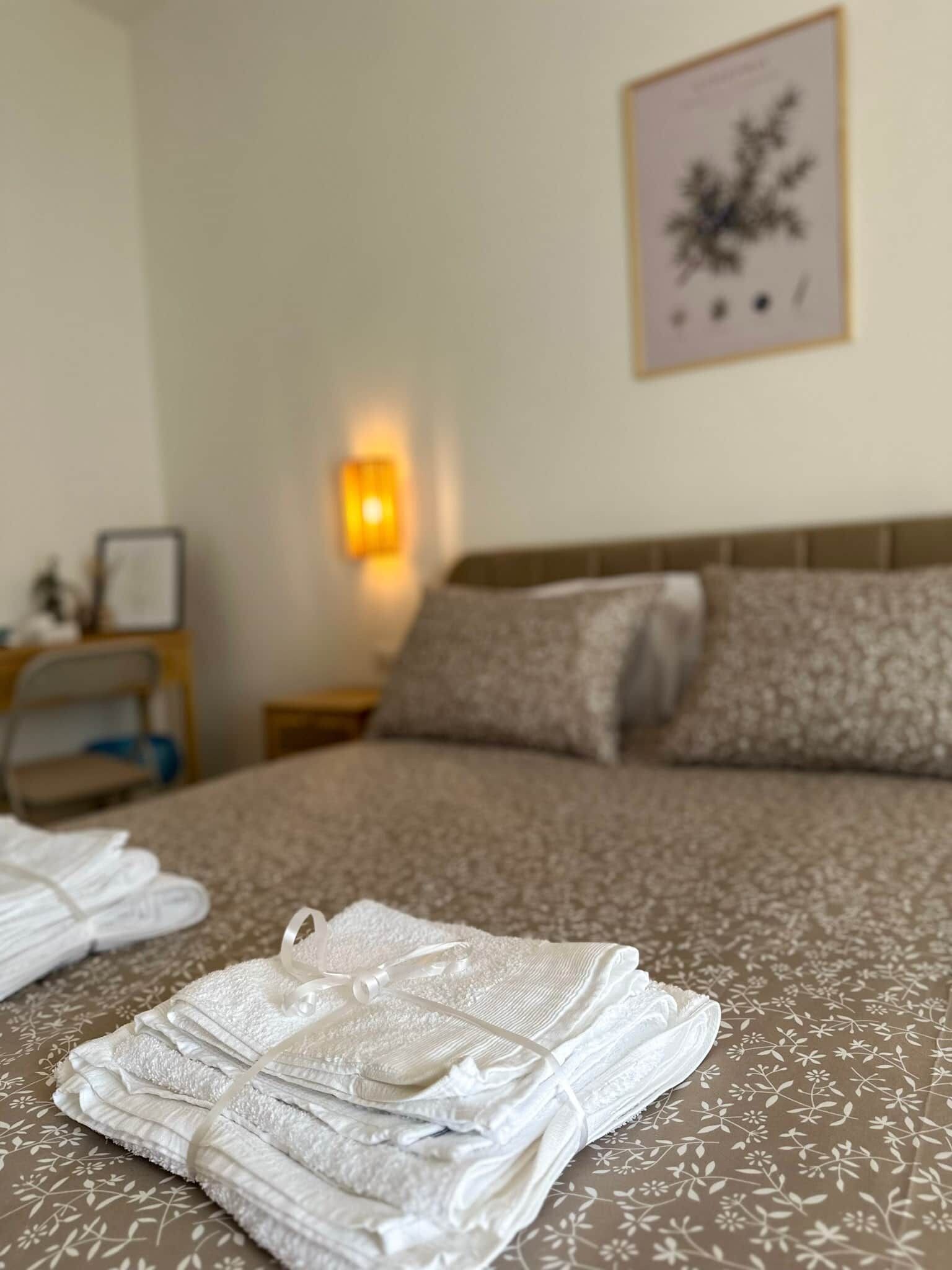 A neatly made bed with a floral bedspread, a bedside lamp, and a framed picture on the wall.
