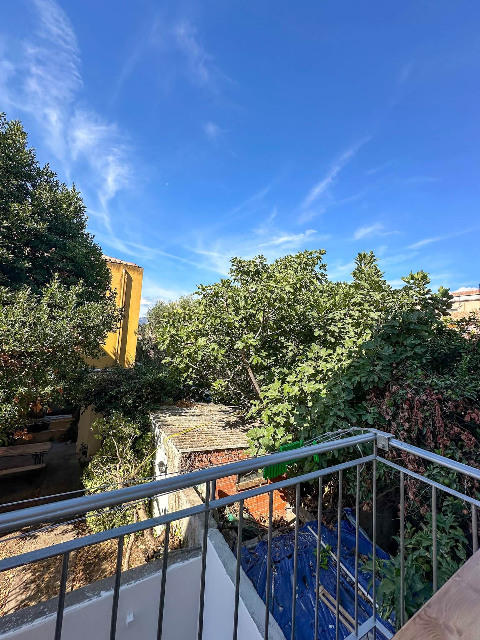 A balcony with a metal railing overlooking a courtyard with trees and a building.