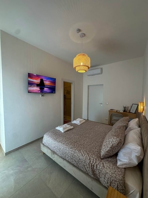 Un dormitorio con cama, televisor montado en la pared, puerta y equipo de aire acondicionado.