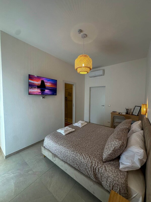 A bedroom with a bed, a television mounted on the wall, a door, and an air conditioning unit.
