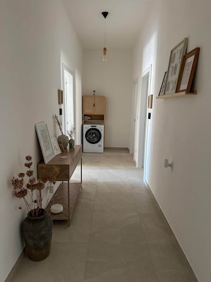 Ein Flur mit einer Waschmaschine, einer Holzbänkl mit Dekoration und gerahmten Bildern an den Wänden.