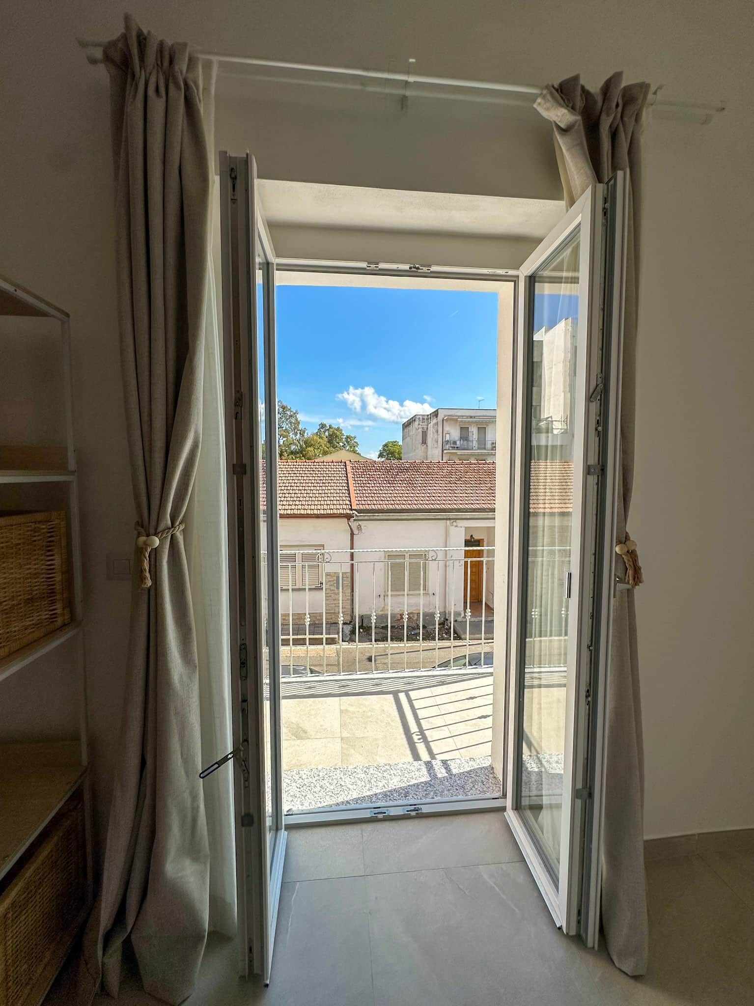Ein Zimmer mit einer Schiebetür, die zu einem Außenbereich mit gefliestem Patio und Blick auf Gebäude führt.