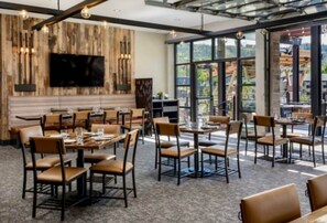Ein Restaurant mit modernem Ambiente, das Holz- und Metallelemente kombiniert, einen Wand-Fernseher und einen Blick ins Freie durch große Fenster bietet.