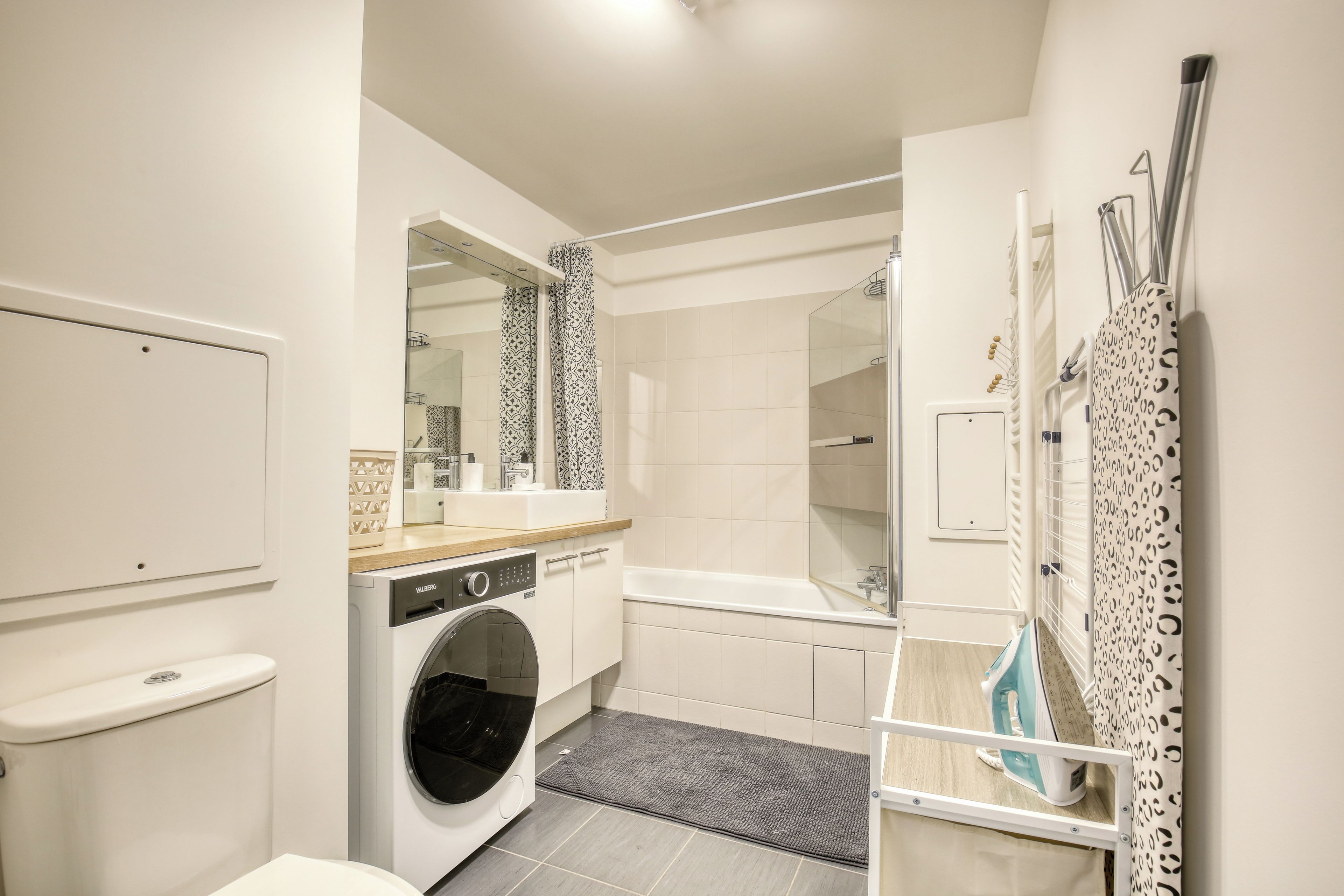 A modern bathroom with a washing machine, a bathtub, and a shower area.