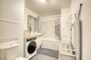 Een moderne badkamer met een wasmachine, een bad en een douche.