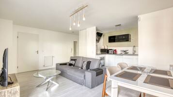Un salon moderne avec un canapé gris, une table basse en verre et un coin repas comprenant une table et des chaises blanches.