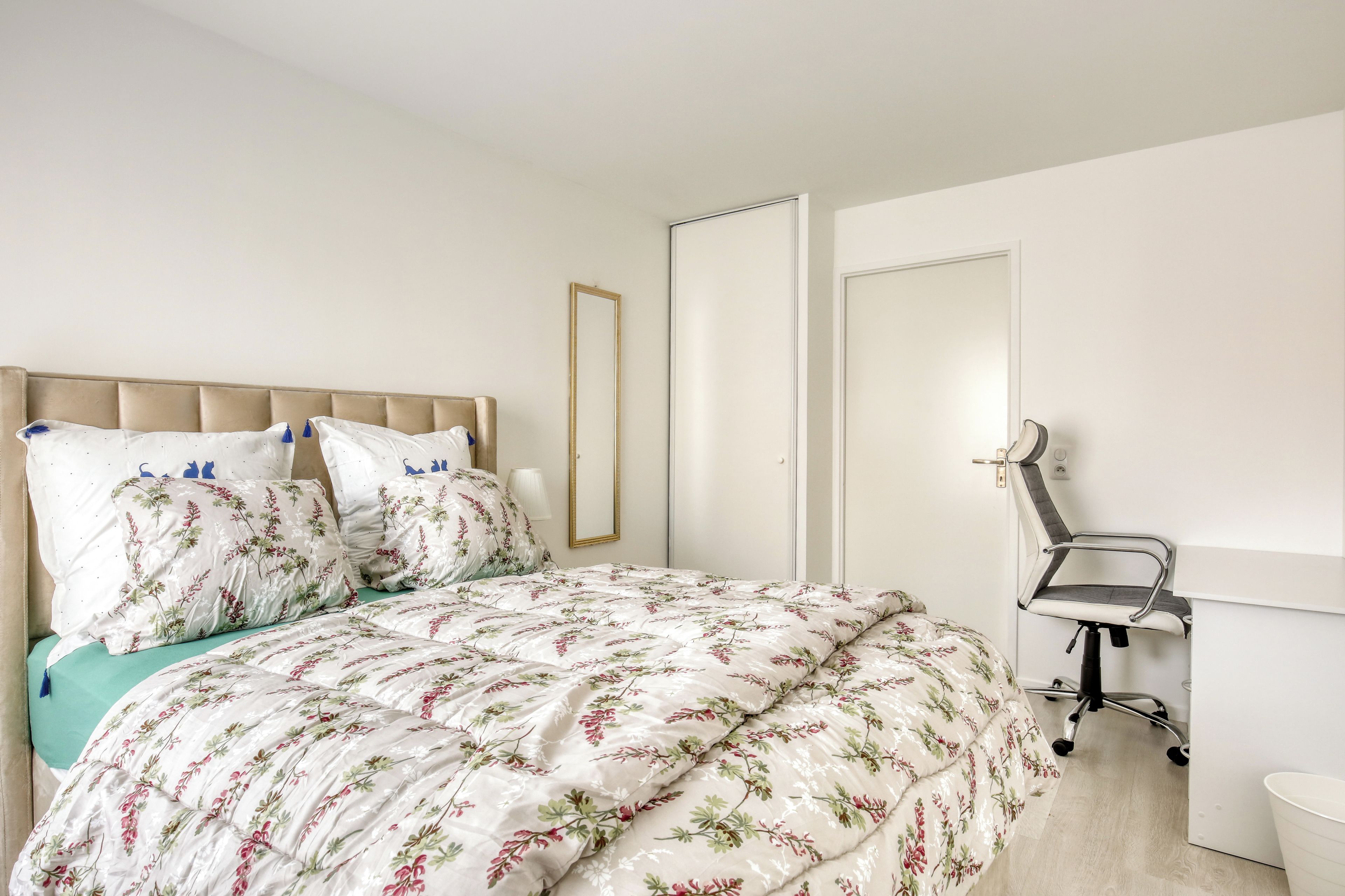 A bedroom with a bed, a chair, a mirror, and a door.
