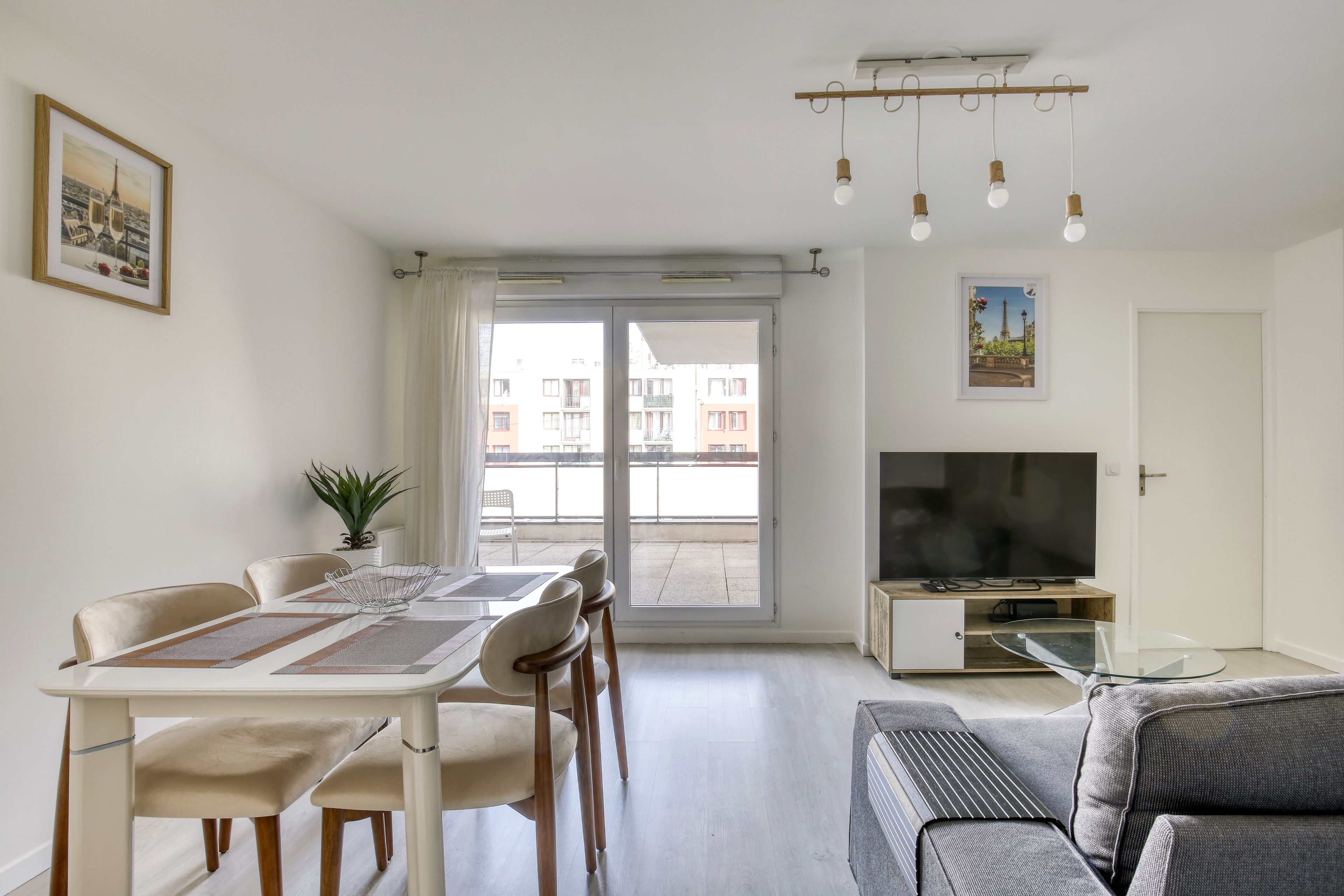 A modern living room with a dining area, a sofa, a TV, and a balcony with a view of buildings.