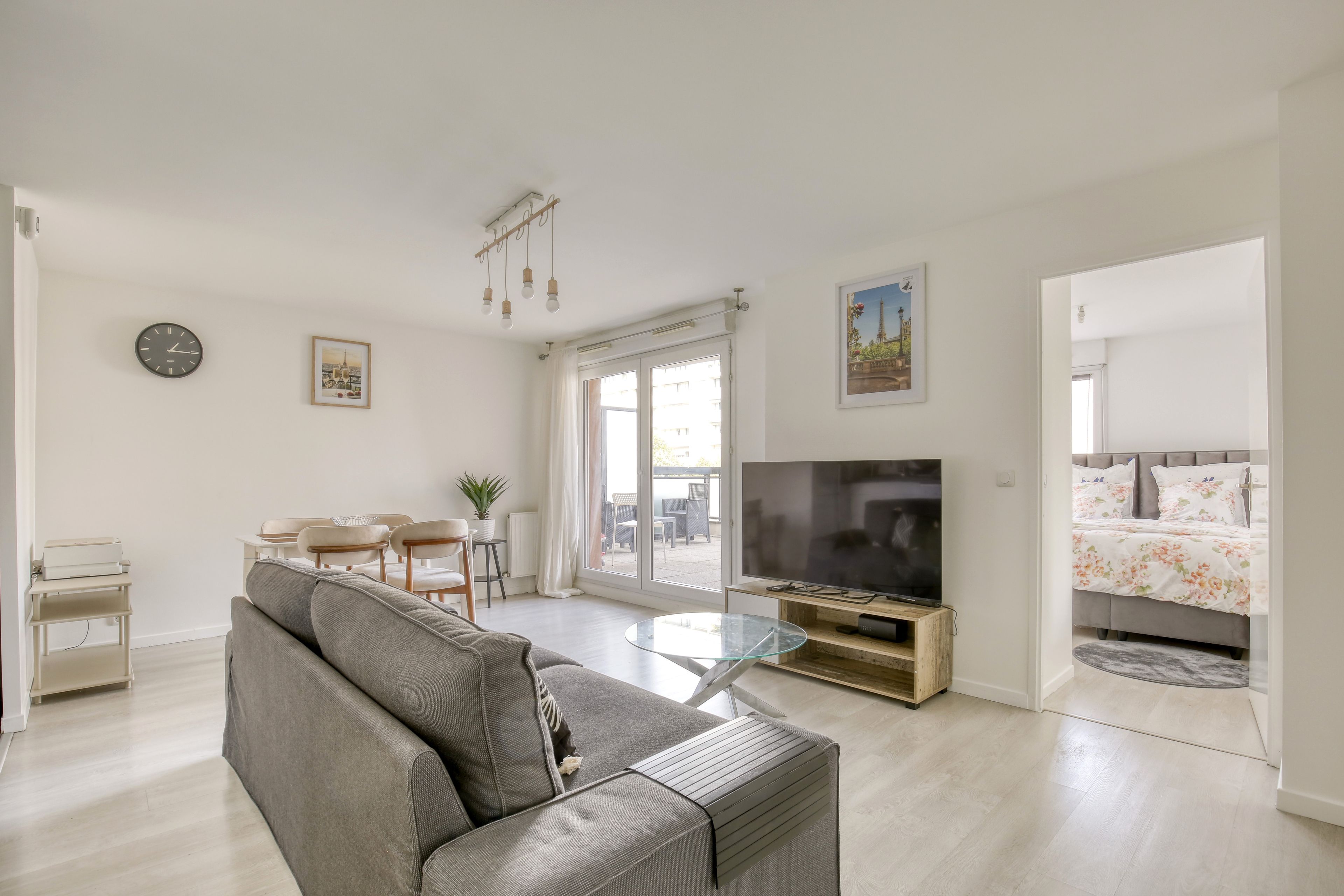 A modern living room with a grey sofa, a flat-screen TV, and a dining area with a table and chairs.