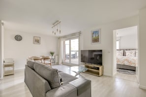 Een moderne woonkamer met een grijze bank, een flatscreen televisie en een eethoek met een tafel en stoelen.