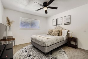 A bedroom with a bed, a ceiling fan, a window with blinds, a bedside table with a lamp, and a rug. - Spacious 4-bedroom house in enjoyable Plano (Plano)