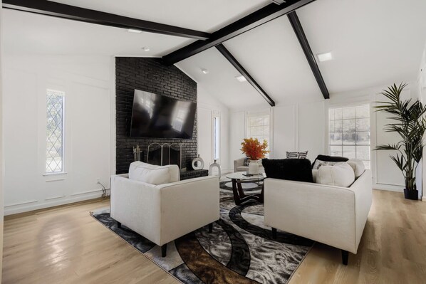 A modern living room with a fireplace, two sofas, a coffee table, and a large TV mounted on a brick wall. - Spacious 4-bedroom house in enjoyable Plano (Plano)